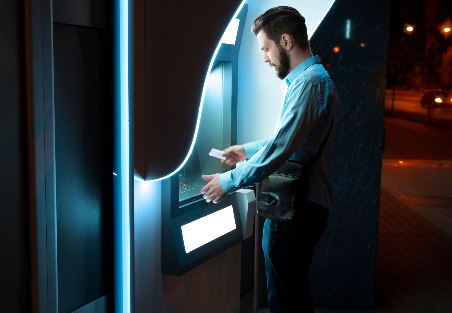 businessman putting credit card in ATM at night